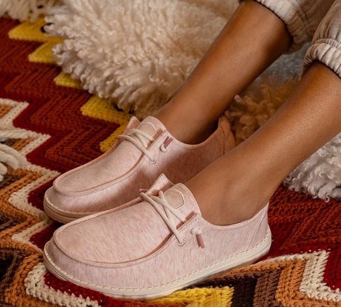 Pink HEYDUDE slip-ons on a woven rug